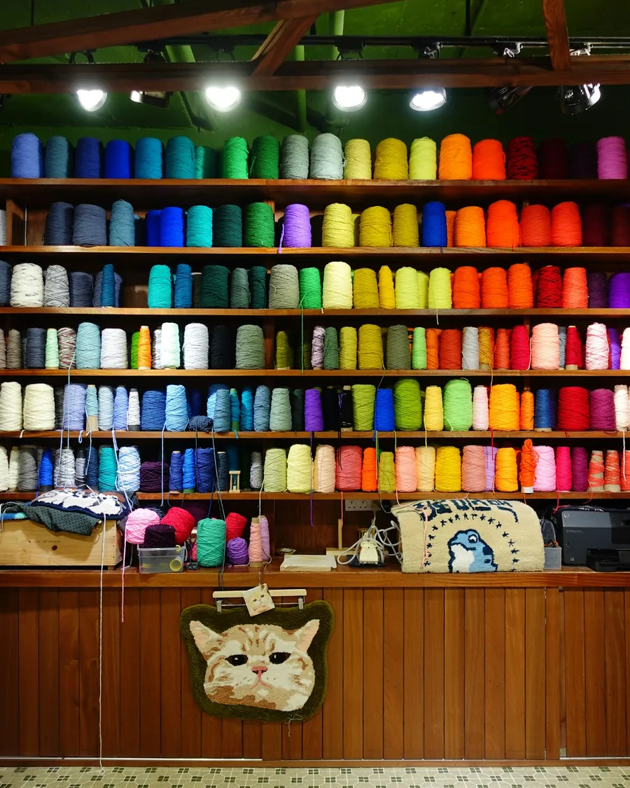 Estantería de taller textil con conos de hilo de muchos colores y piezas tafteadas colgadas debajo